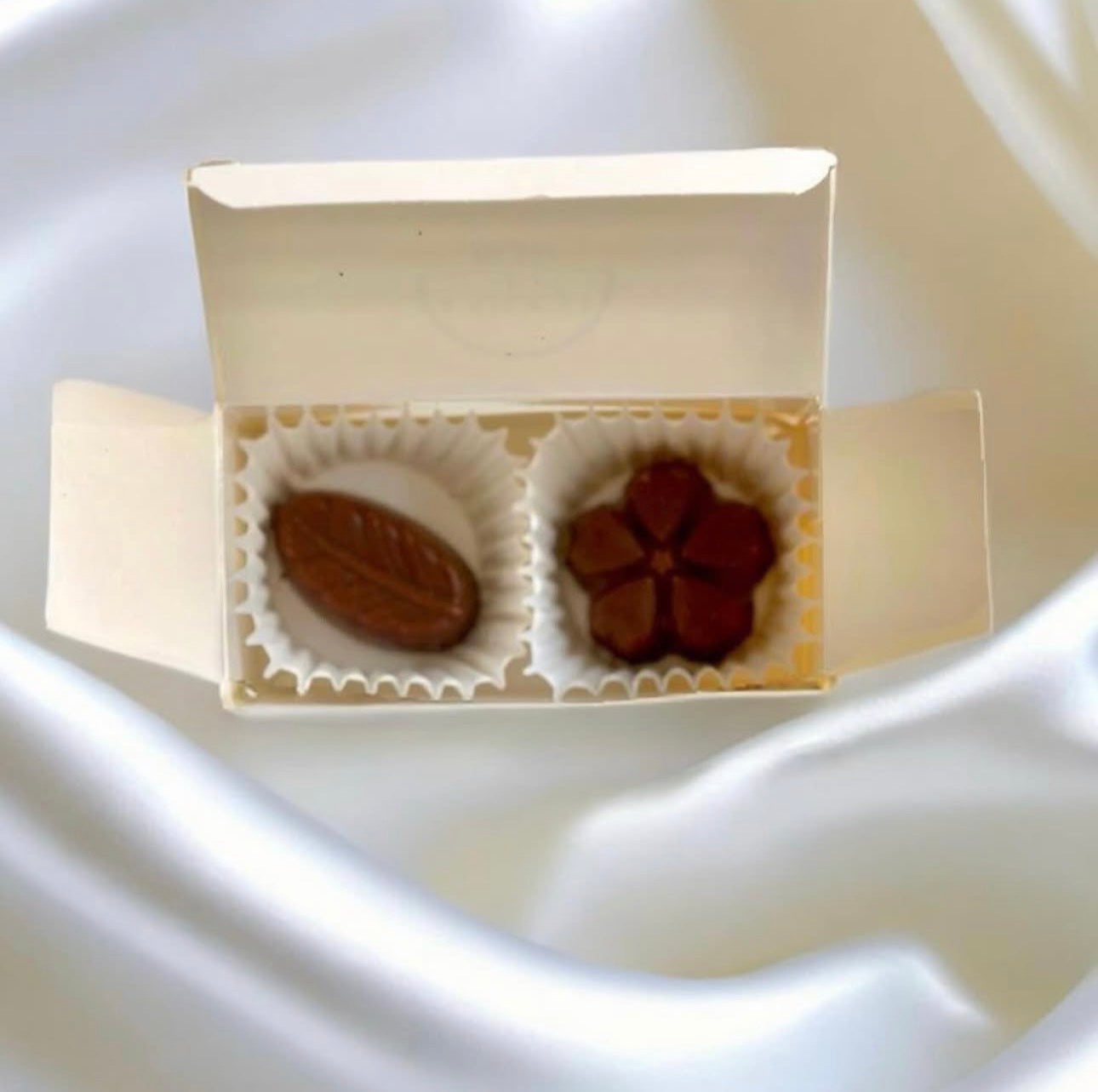 Two chocolates in a small open box on a white surface