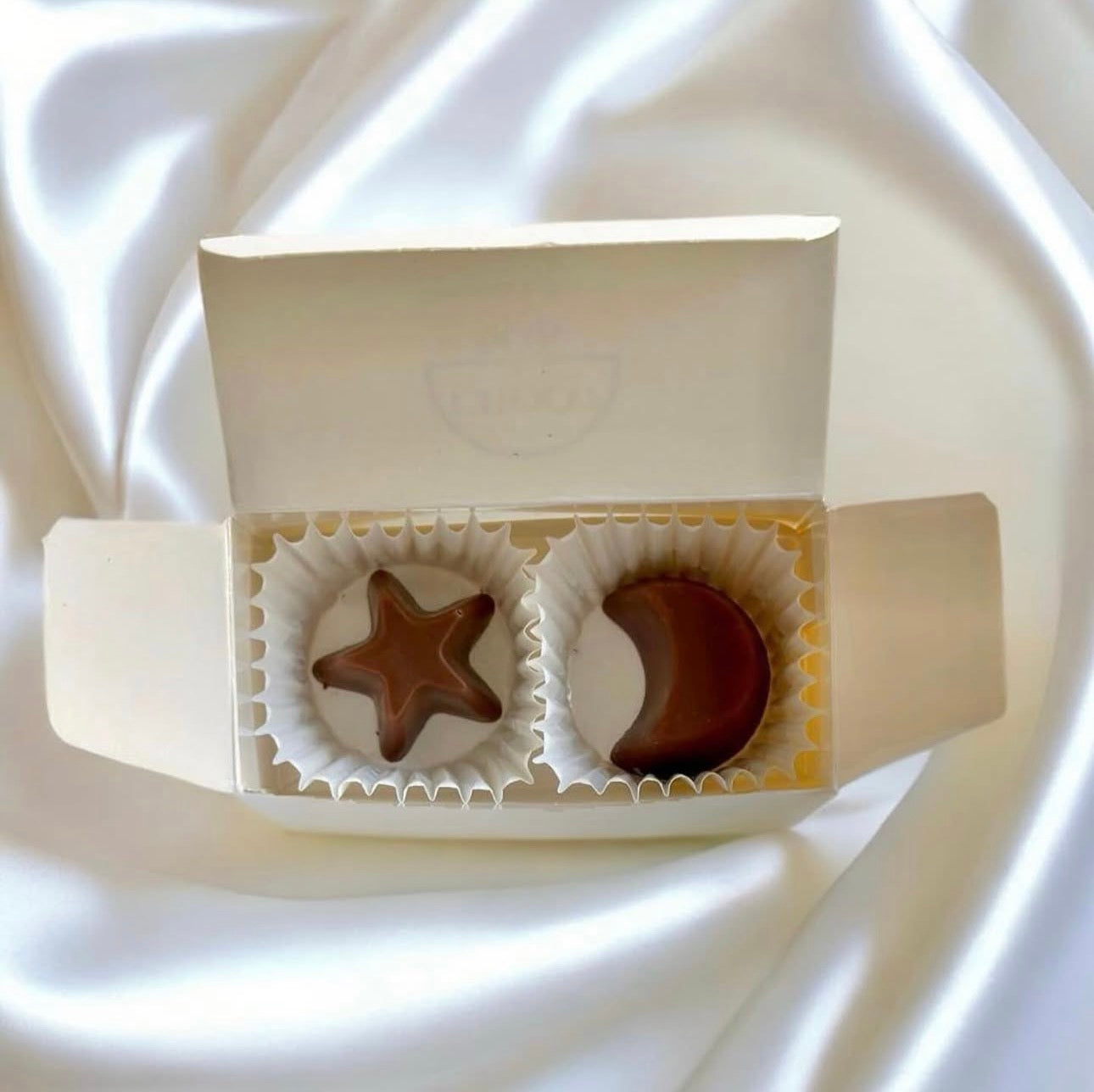 Two chocolates in a white box on a white fabric background