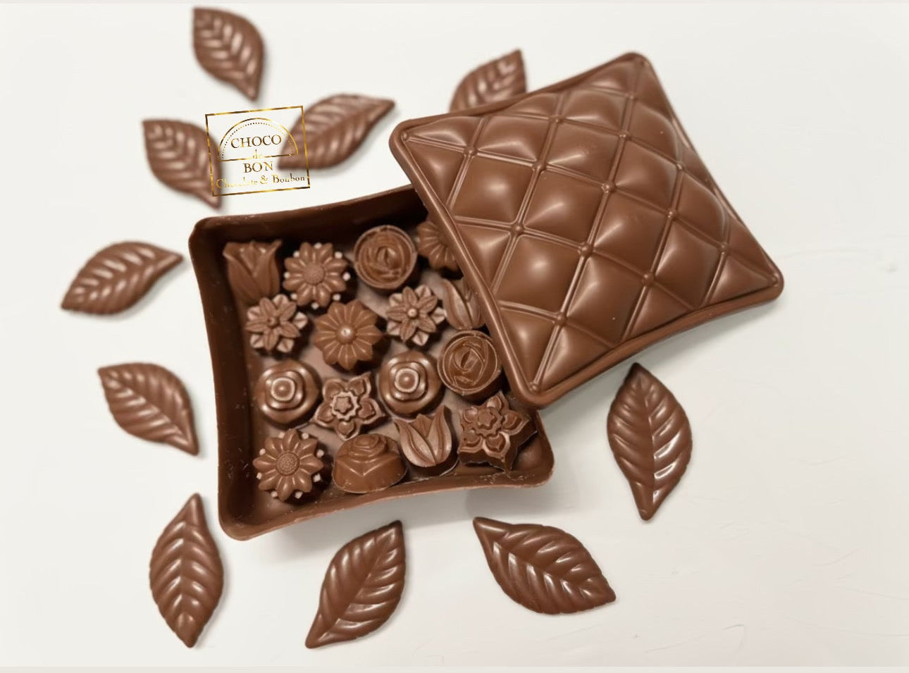 Chocolate box with floral bonbons and leaves on a white background